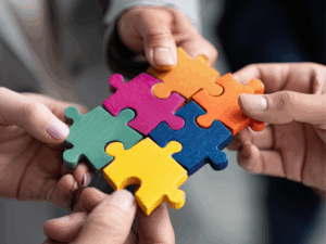 Manos colaborando para ensamblar piezas de puzzle de colores vibrantes, representando trabajo en equipo y colaboración en ecosistemas de innovación