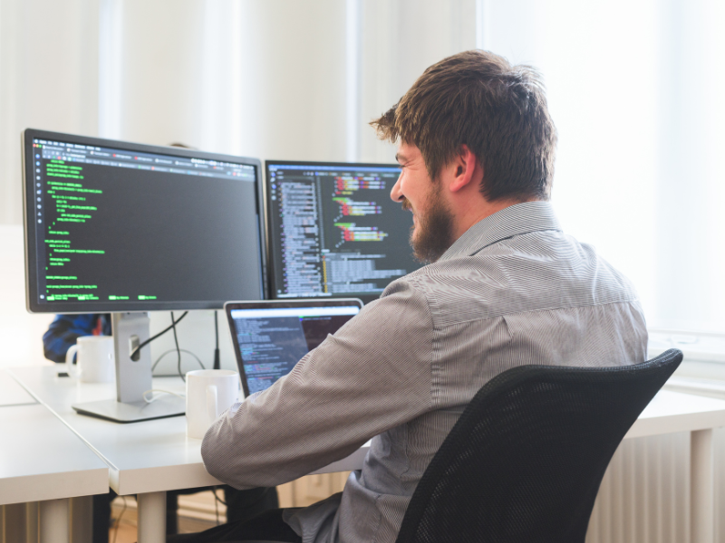 Desarrollador profesional trabajando con código en múltiples monitores en oficina moderna, representando desarrollo tradicional versus plataformas no-code empresariales
