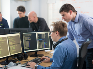 Equipo de desarrollo de software trabajando frente a varios monitores con código en una oficina moderna