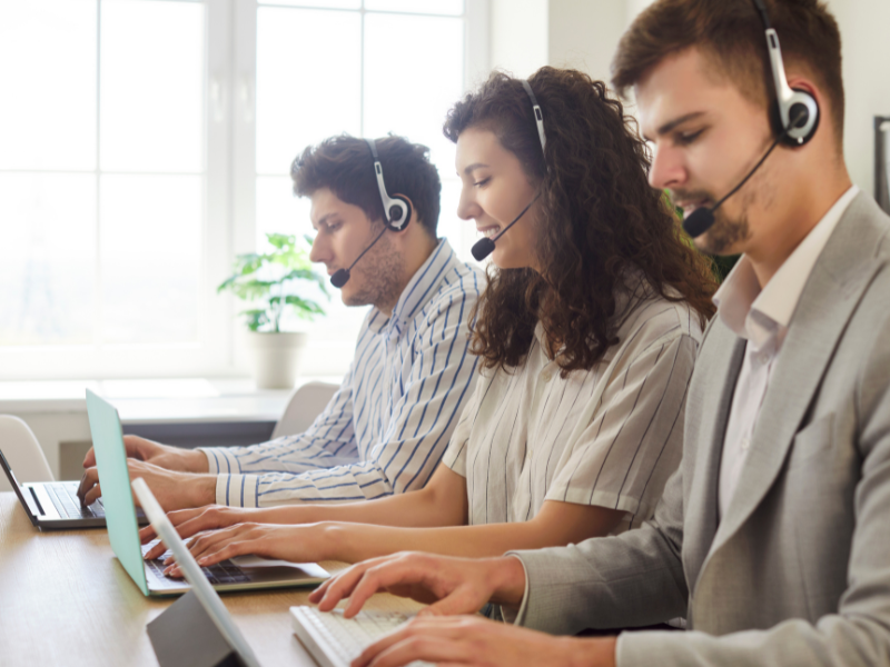 Equipo de atención al cliente con audífonos trabajando en computadores portátiles en una oficina luminosa
