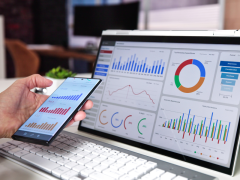 Ejecutivo monitoreando métricas de negocio en smartphone frente a dashboard de analítica en pantalla