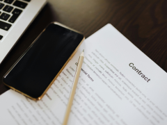 Contrato de servicios tecnológicos con cláusulas comerciales sobre escritorio junto a teléfono y laptop